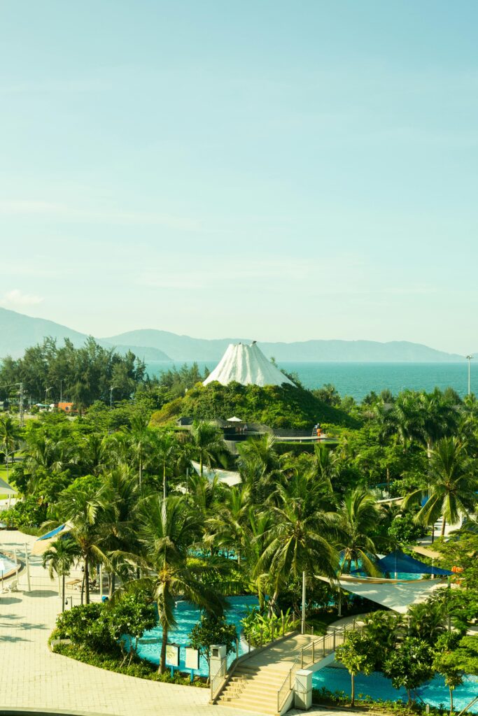 Aerial view of a lush tropical landscape with a distinctive architectural structure and ocean backdrop.