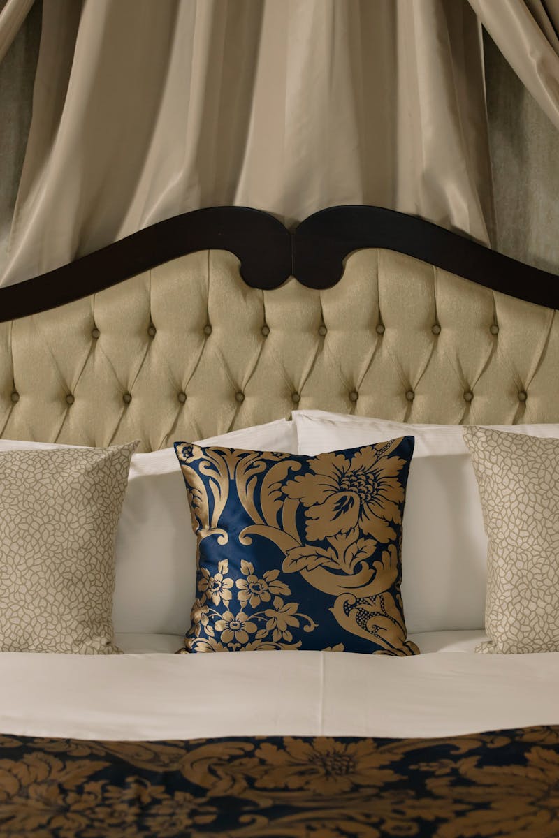 Elegant hotel room with plush headboard, decorative pillows, and luxurious curtains.